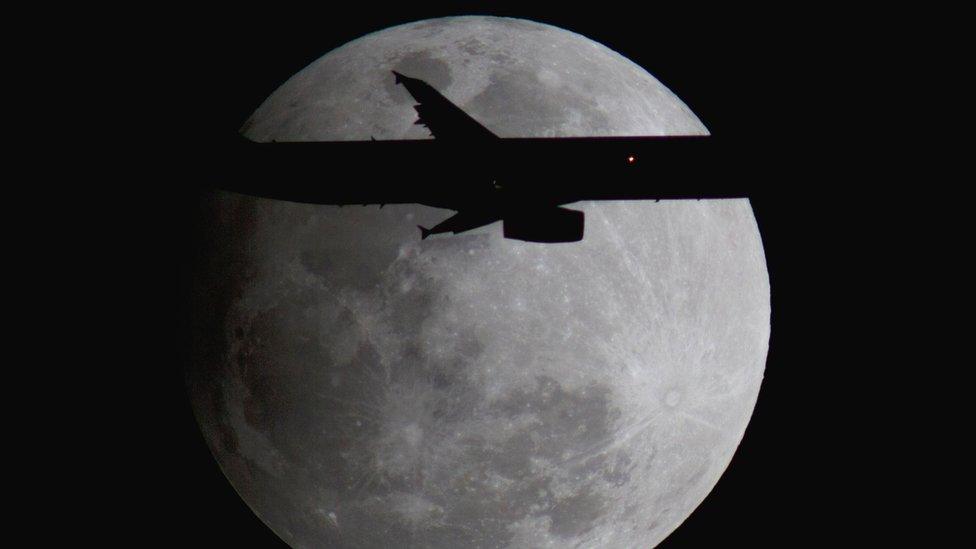 An Airbus passenger jet on final approach to Orlando International Airport transits past a full "snow" moon during the penumbral eclipse on February 10, 2017.