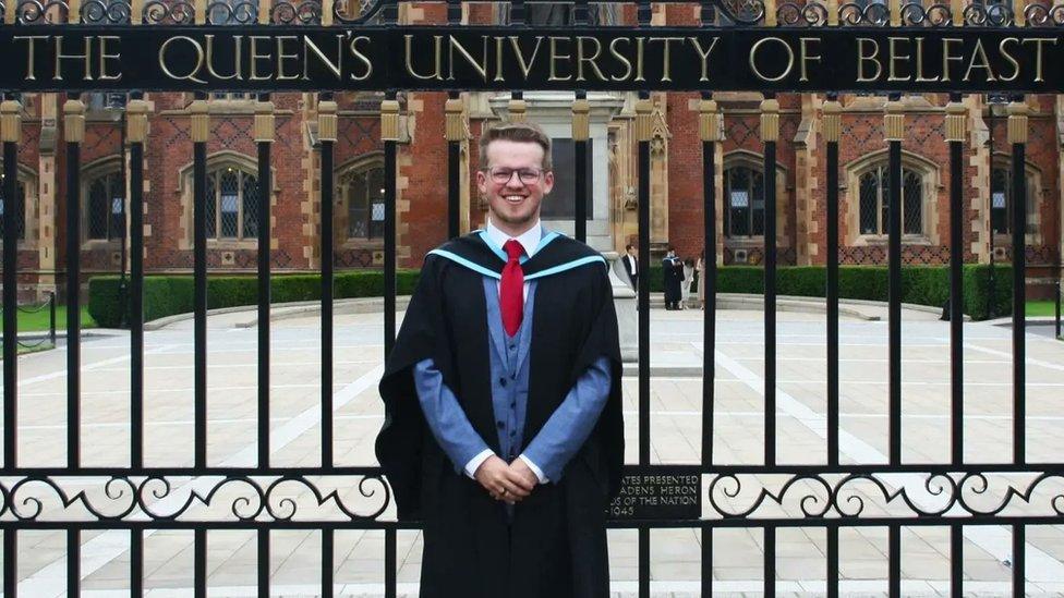 Dr Tim Neill stands at the gates of Queen's University Belfast on the day of his graduation