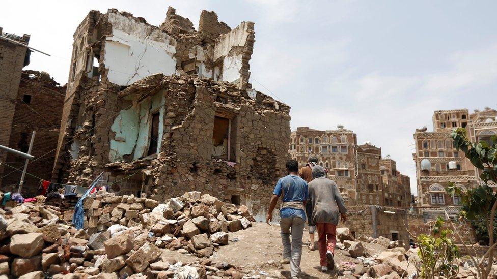 People walk past a house destroyed by an air strike in the Old City of Sanaa, Yemen (8 August 2018)