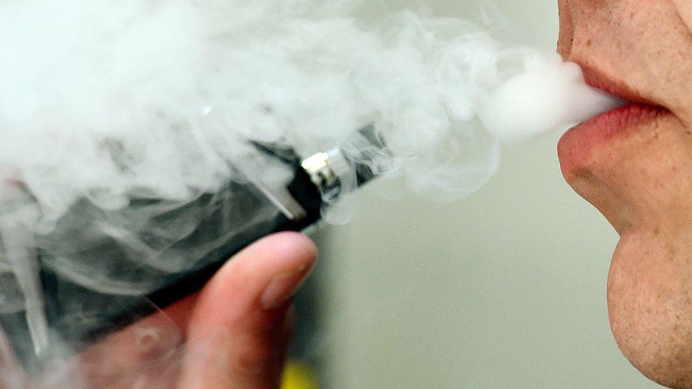 Close-up of a person's lips surrounded by smoke as they exhale from a vape held close to their mouth