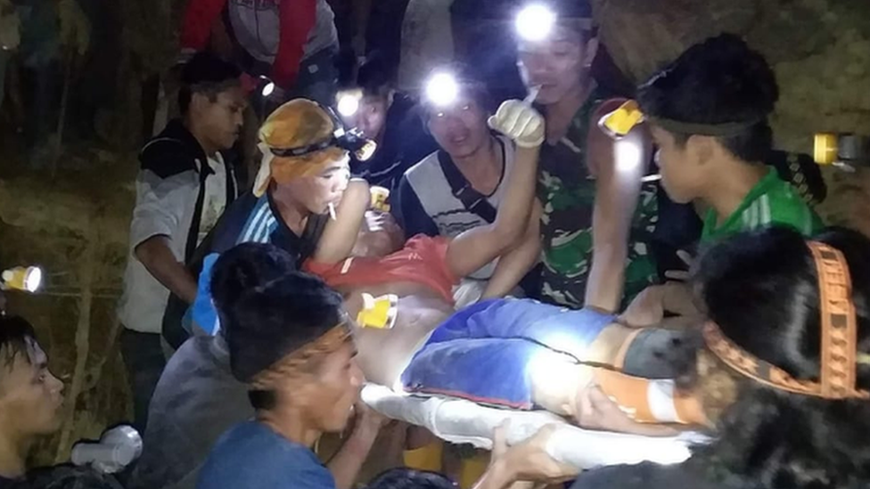 Rescuers from Indonesia's national disaster mitigation agency, the BNPB, carry a survivor off a muddy hillside with the help of head-torches