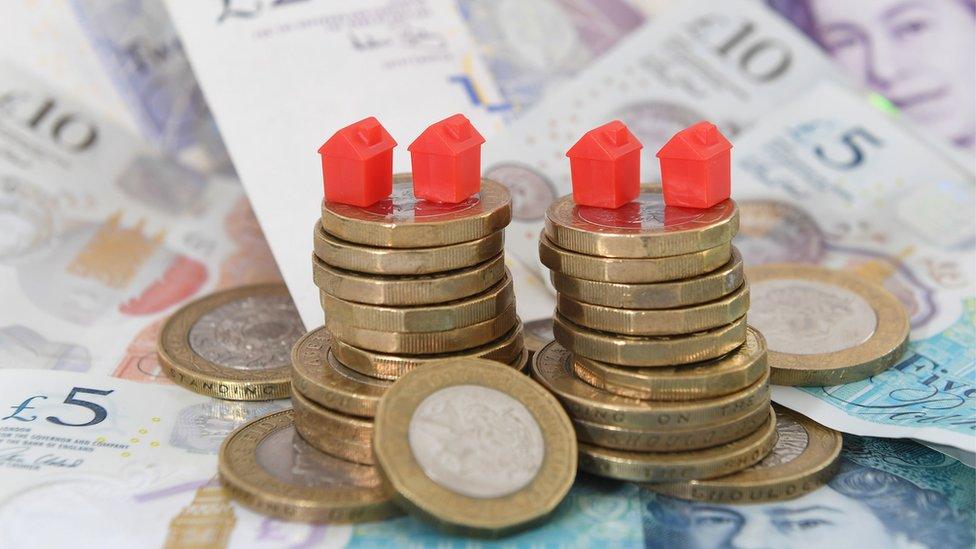 Model houses on a pile of British sterling coins and bank notes