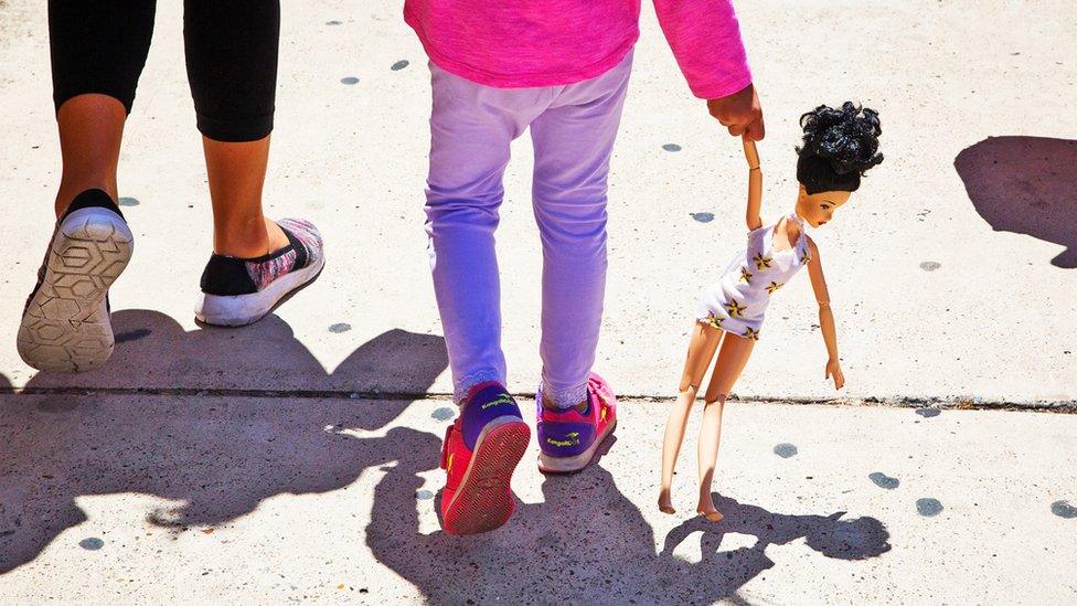 A girl holding a doll by the arm walking next to adult