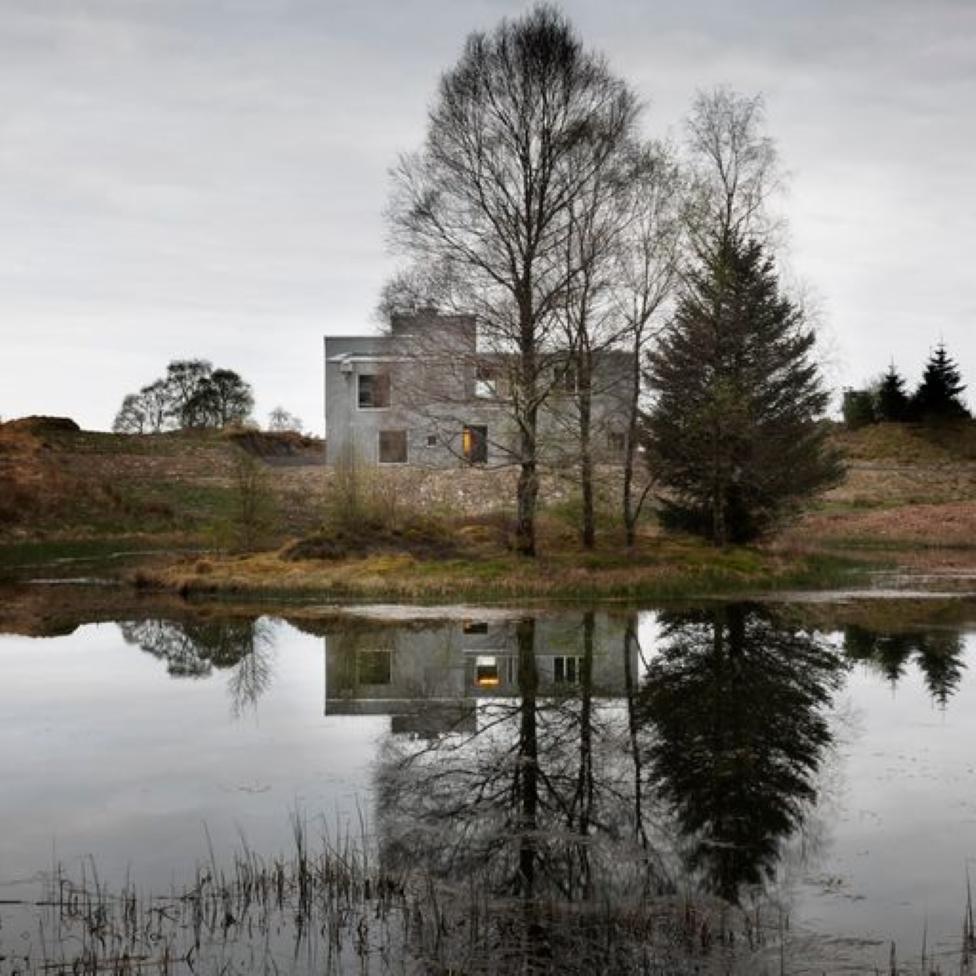 The grey, brutalist home stands close to a pond.