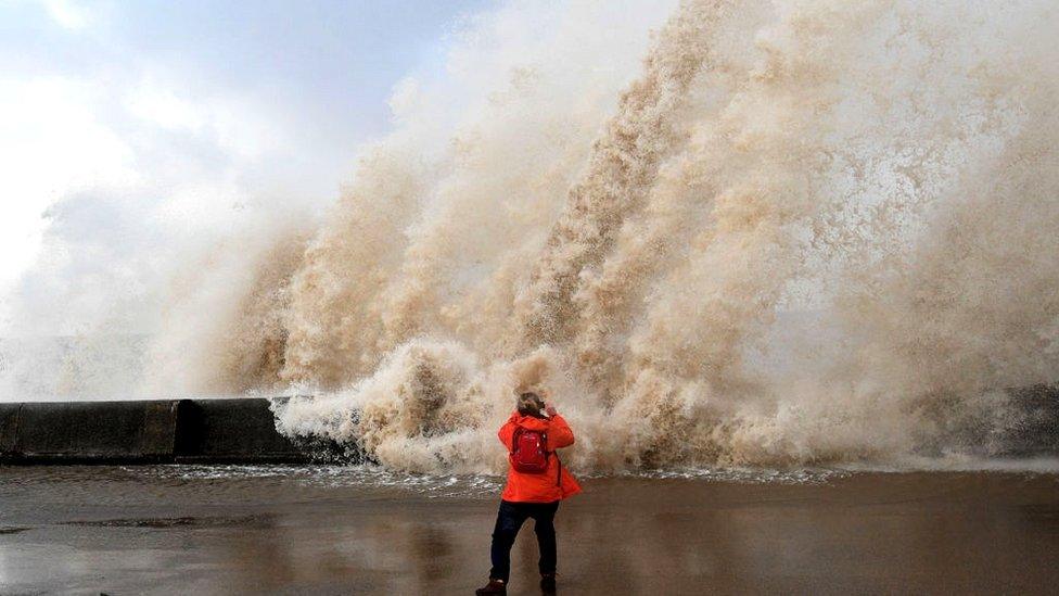 a woman takes a picture of a huge wave