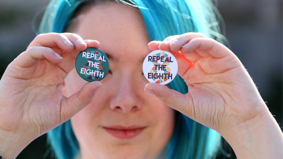 A woman holds 'repeal the eighth' badges up in front of her eyes at a pro-choice rally