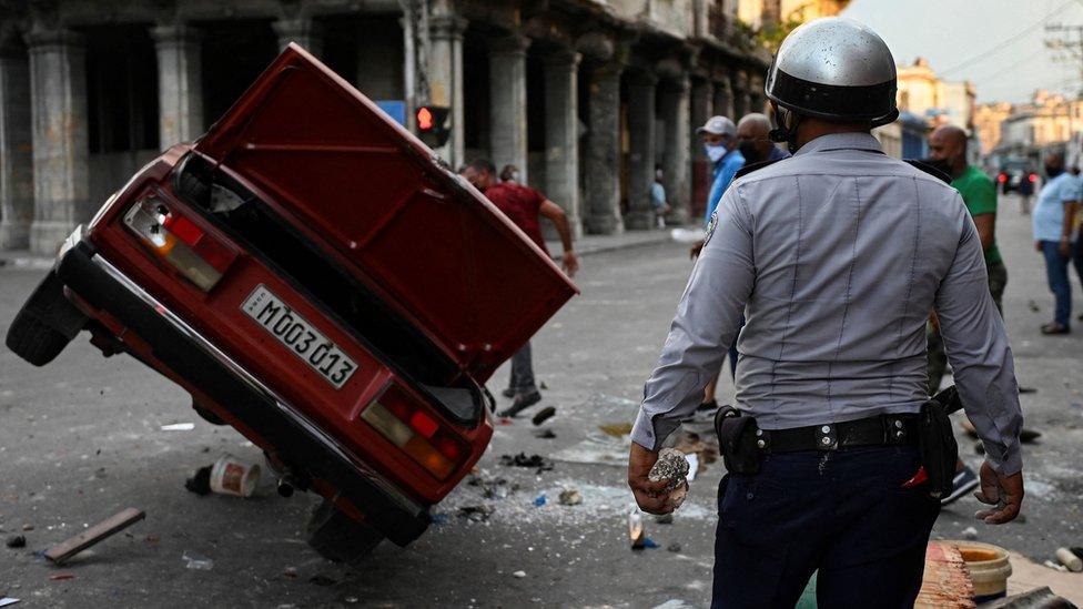 A policeman watches a police car overturned during a demonstration against Cuban President Miguel Diaz-Canel in Havana, on 11 July 2021.