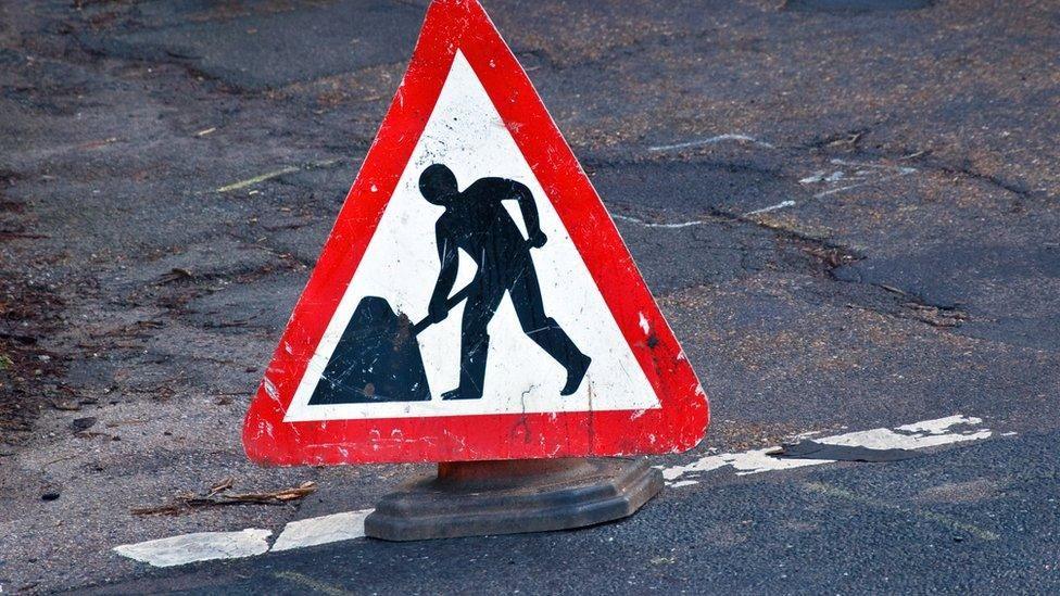 A red and white triangular road sign signalling resurfacing works are being carried out on the road ahead.