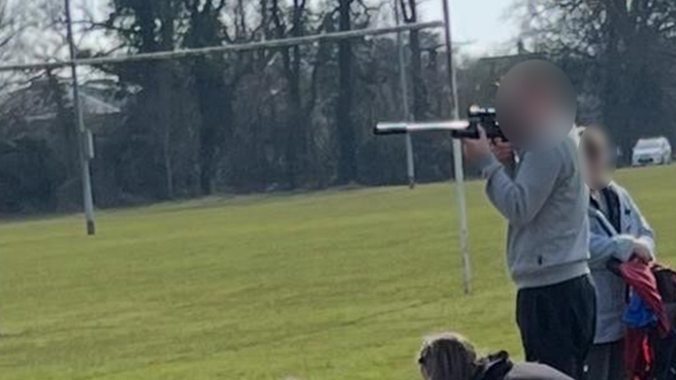 A man in a grey jacket at a pitch side looking down a barrel-like fitting on the device on a football pitch. 