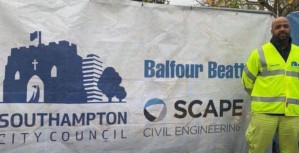 A roadworker standing infront of a sign highliting Southampton City Council's partnership with roadworks operator Balfour Beatty and civil engineering firm Scape.