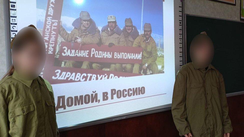 Ukraine students, from another school, standing next to a screen which says, ‘Homewards to Russia’