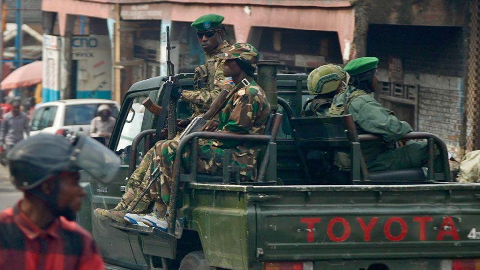 Four M23 fighters in uniform, some in green berets, holding guns on the back of a green Toyota truck seen in traffic in Goma, DR Congo - February 2025