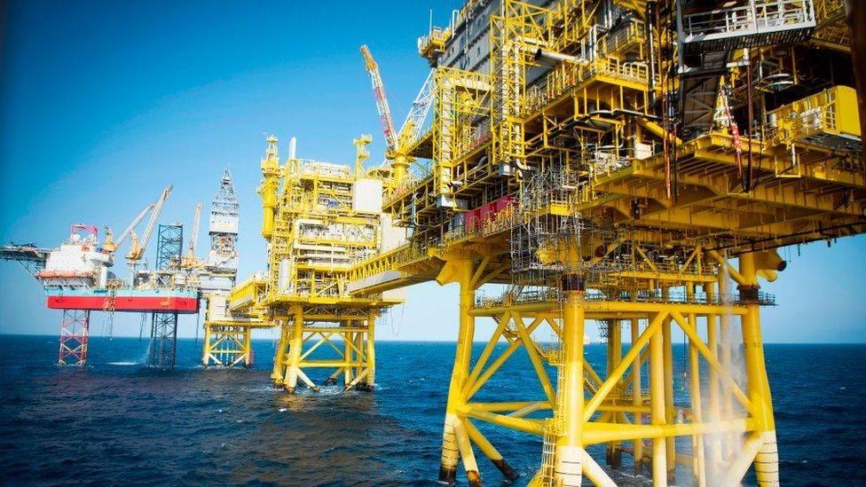Image of an oil rig in the north sea - yellow stanchions reach down in the water from several platforms, against a blue sky and deeper blue sea