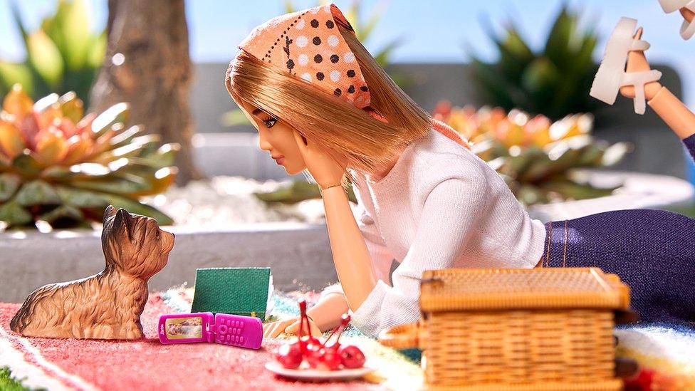 a barbie doll looking at her dog with a small flip phone by her hand