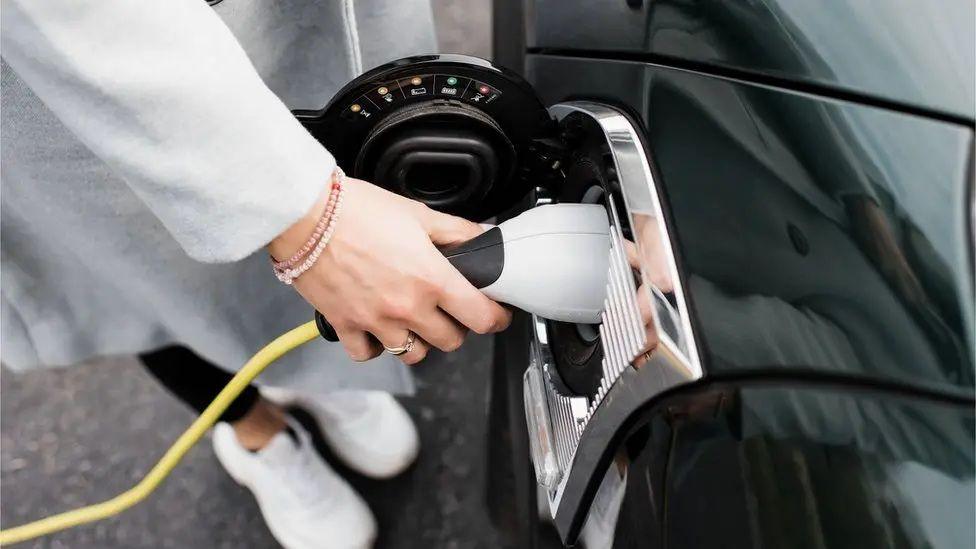 The picture shows a woman's hand plugging an electric charger into a black car