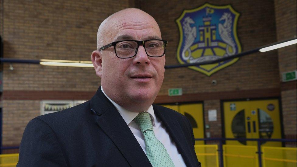 Man standing in a school wearing glasses looks at camera