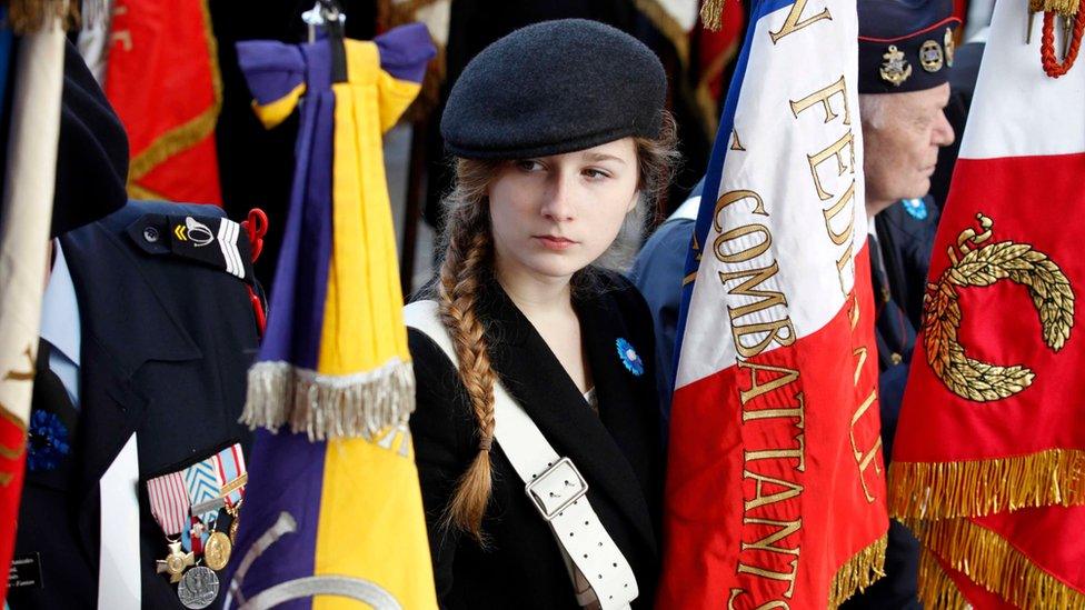 Charlotte, the niece of a French veteran, holds a French veterans flag at the tomb of the unknown soldier during the Armistice Day ceremony in Paris