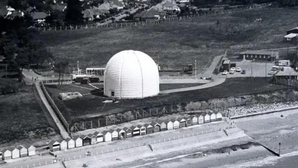 Black and white aerial image of the radar station behind a row of beach huts