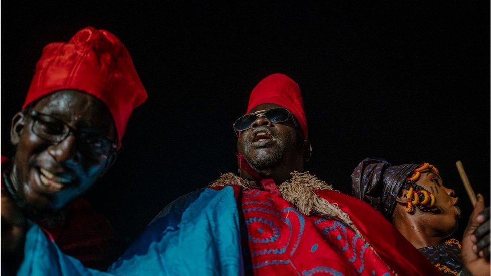 Two men wearing colourful traditional clothing singing and smiling