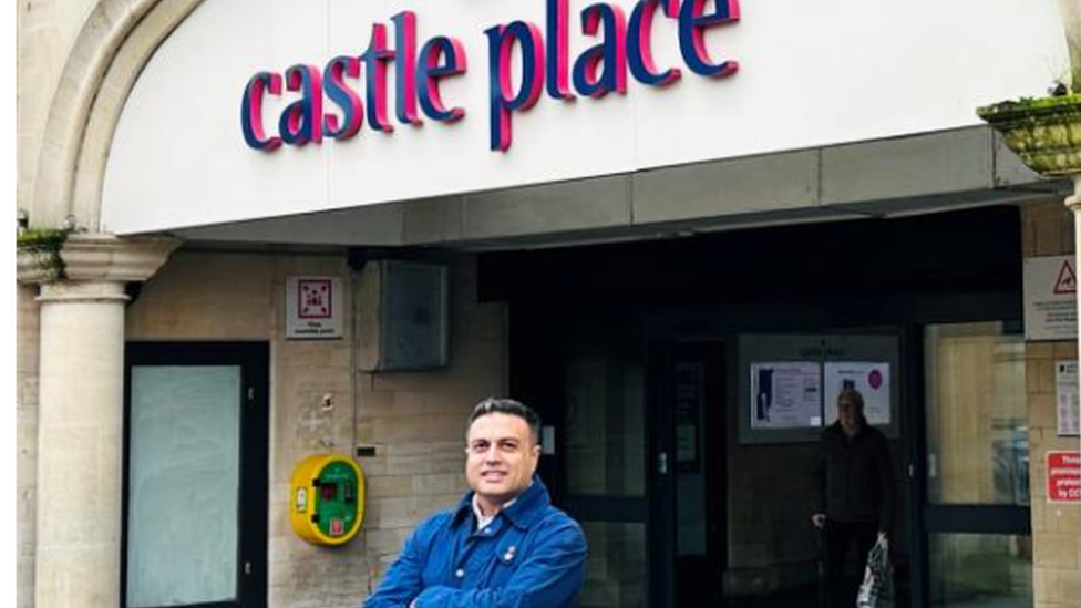 Tahir Ali smiling with arms folded across his chest, while standing outside Castle Place Shopping Centre