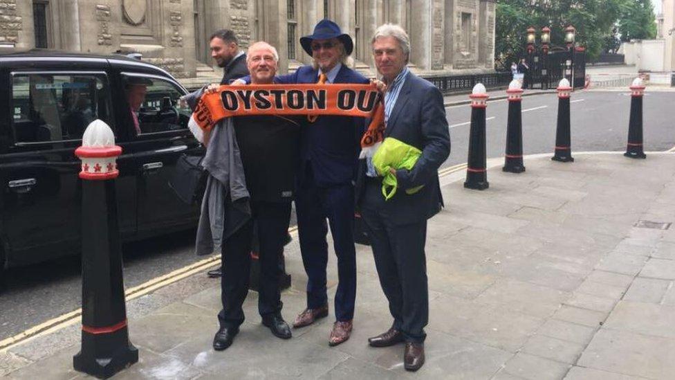 Owen Oyston (centre) poses outside the court holding a protester's "Oyston Out" Blackpool scarf