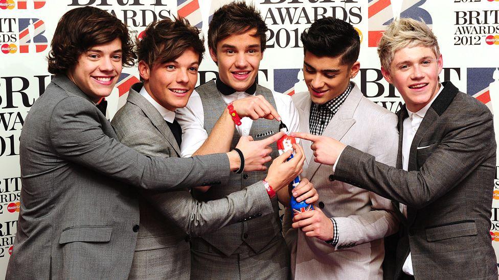 One Direction all holding and pointing to a Brit Award in 2012