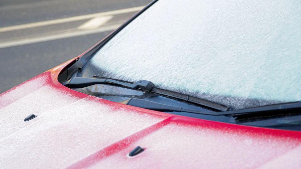 A red car with a frosty windscreen.