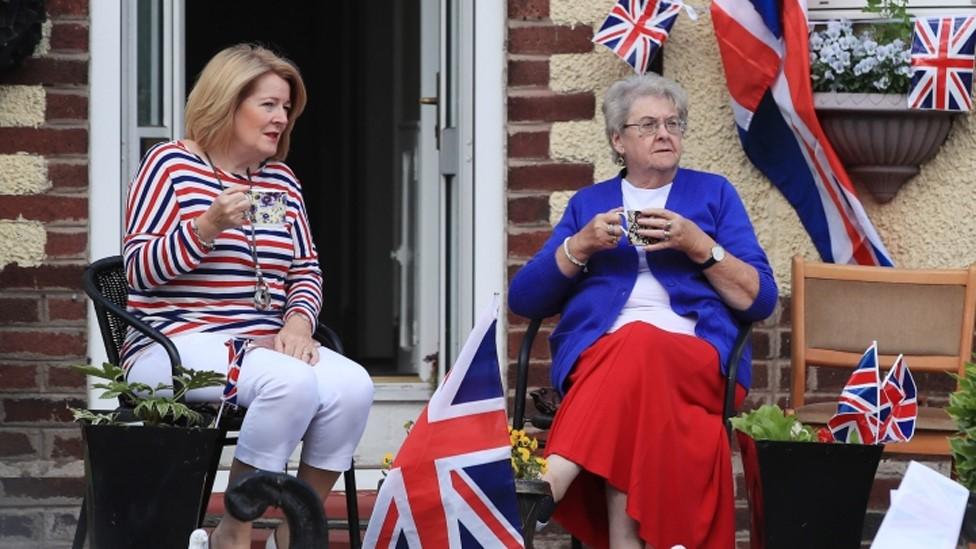 Two women sit outside a decorated house near Runcorn Station