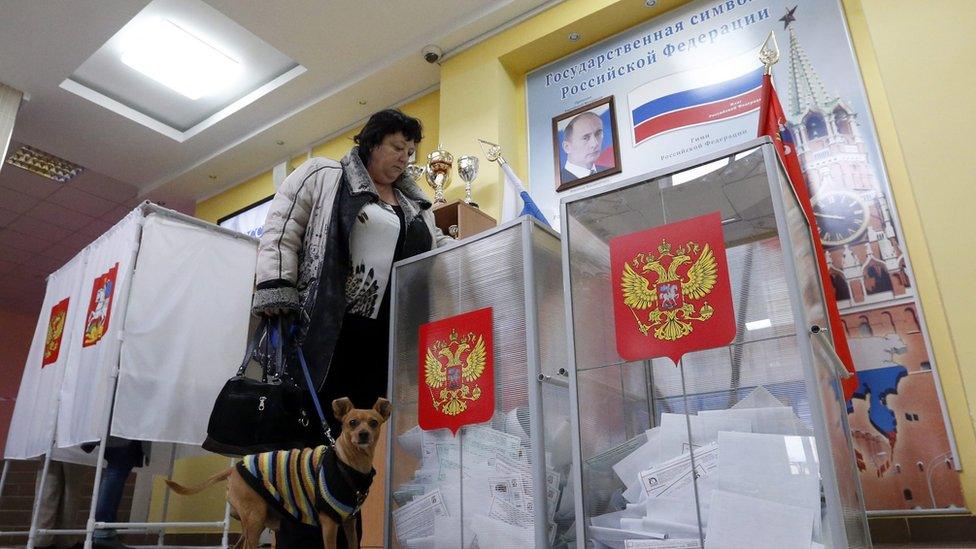 A woman casts her ballot in front of portrait of Russian President Vladimir Putin at a polling station at a local school in Moscow, Russia