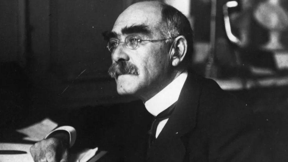 A black and white photo of Rudyard Kipling wearing a suit. He has round glasses, a moustache and bushy eyebrows