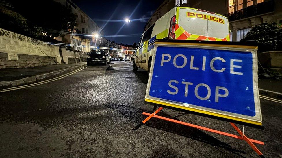 A Police Stop sign in front of a police van and police tape in the background