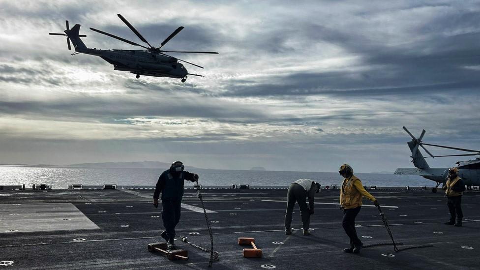 A helicopter flies above the ship's deck