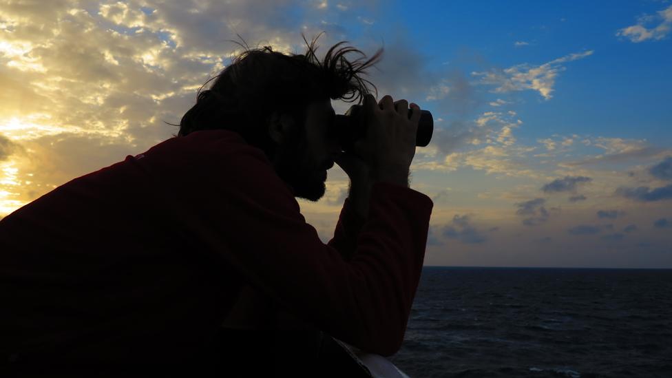 Volunteer looks out to sea through binoculars