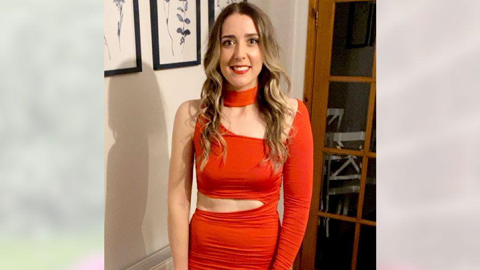 Vicky Green is smiling while wearing a red dress. She has long blonde hair.