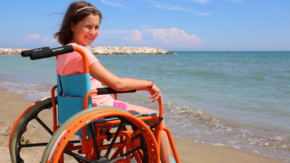 Girl using a wheelchair on beach looks out to sea