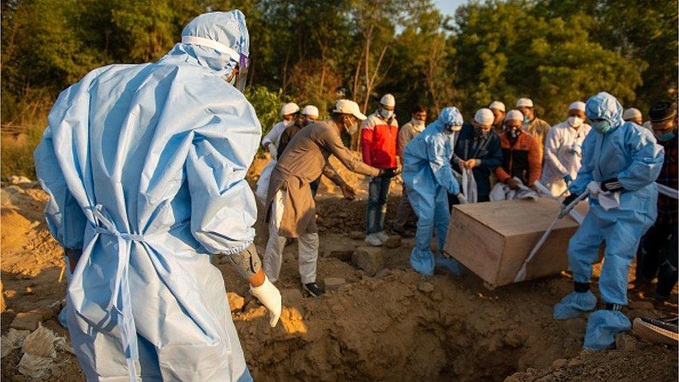 Muslim Volunteers wearing protective suits from Jamiat Ulama-i-Hind ( Socio-Religious organization of Indian Muslims) along with relatives lower the body of a covid-19 victim for burial at a graveyard