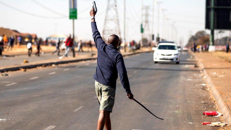 A man fires a hand gun in the air to disperse a mob of alleged looters outside of the Chris Hani Mall in Vosloorus, on July 14, 2021