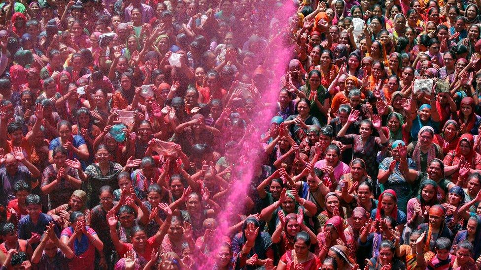 A crowd prays as they are sprayed with colours by a priest