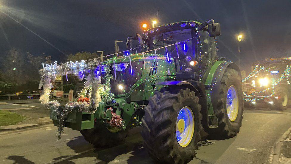 A green tractor covered in multi-coloured Christmas lights and tinsel.