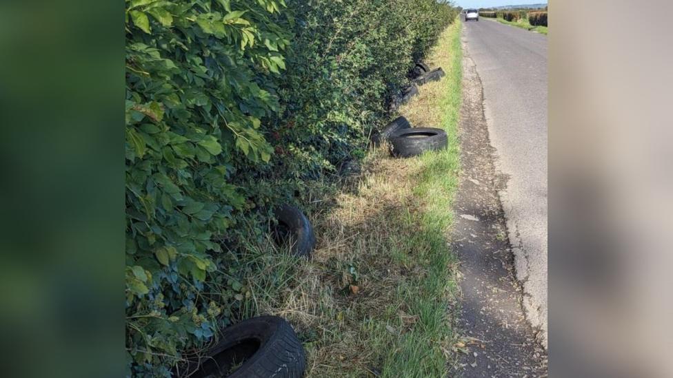 Tyres in a ditch with view of a country lane