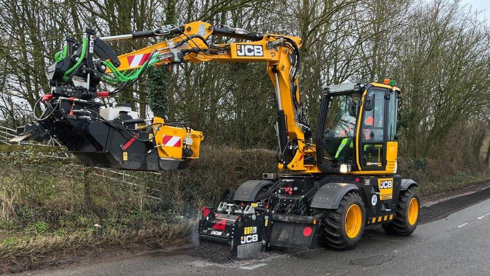 Yellow machine resembling digger with its claws raised on a road