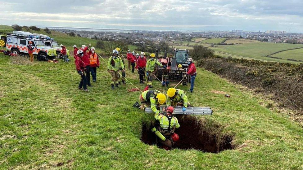 A rescuer is lowered into the sinkhole