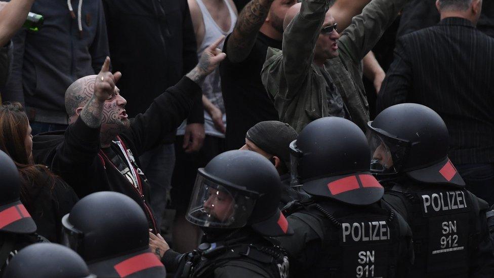 Right wing protesters gesture towards police in riot gear as they gather at the place where a man was stabbed