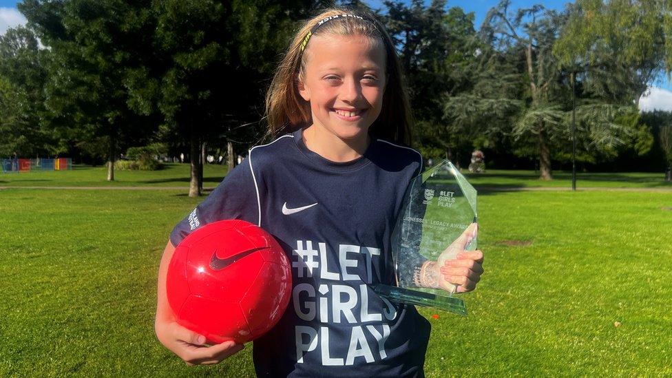 Lola holding a red football and her Let Girls Play award