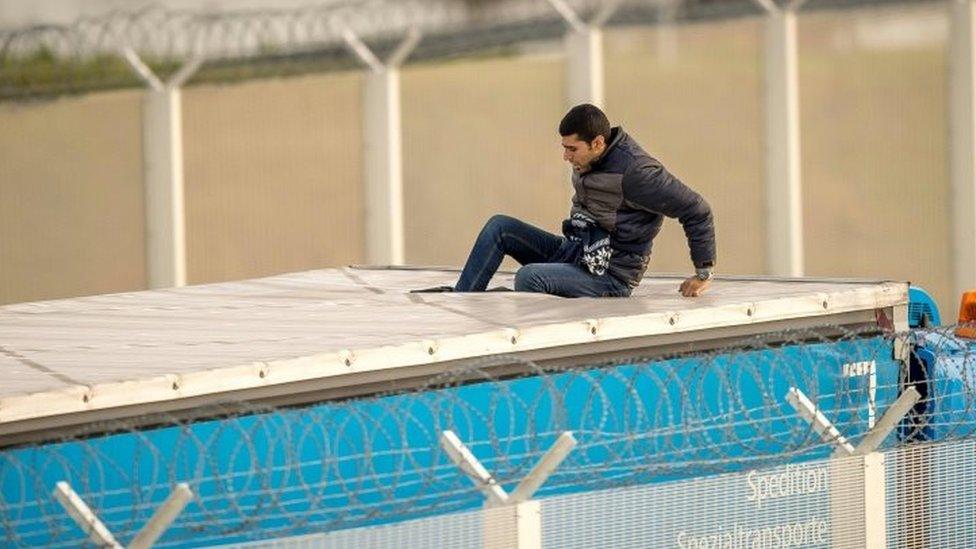 A migrant entering the trailer of a truck after having cut the tarpaulin roof at the Eurotunnel site in Calais