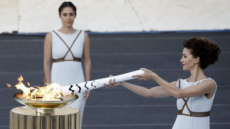 Greek actress Katerina Lehou (R), lights an Olympic torch during the handover ceremony, April 27, 2016