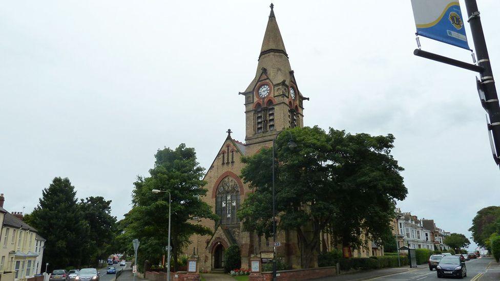 A view of the Hornsea United Reformed Church, which is built from yellow brick and has a pointed steeple containing a clock