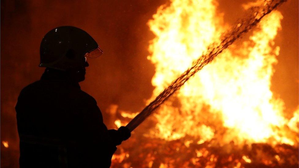 A silhouette of a fire fighter dampening down a building