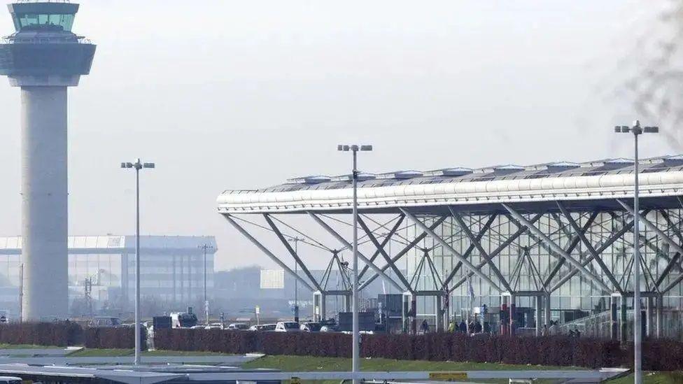 Stansted Airport pictured from the outside showing the control tower and terminal. All is fairly grey and glass.