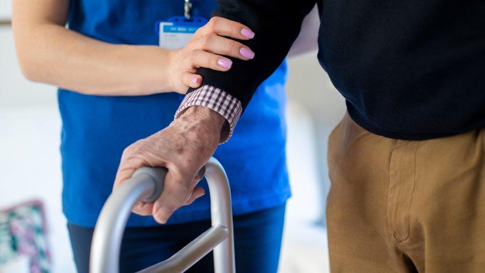 Care home worker helping man with walking frame